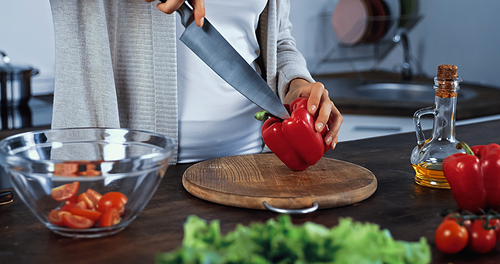 Cropped view of woman holding knife and bell pepper near vegetables on blurred foreground