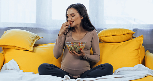 Pregnant woman eating fresh salad on couch