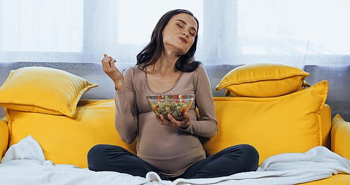 Pleased pregnant woman eating fresh salad in living room