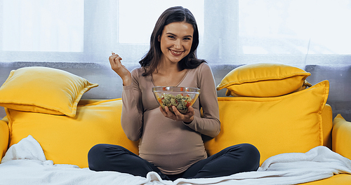 Smiling pregnant woman holding bowl with fresh salad