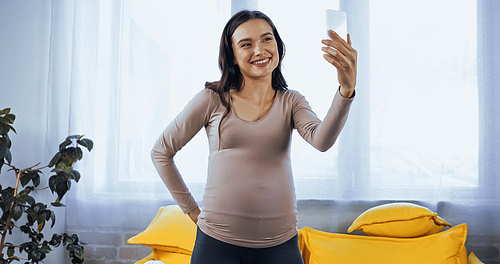Pregnant woman smiling at smartphone during video call