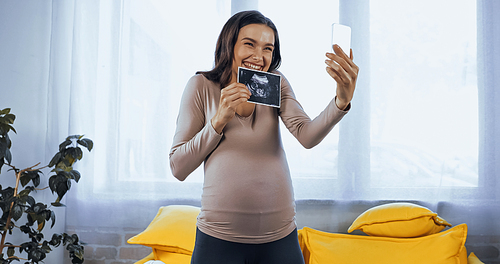 Cheerful pregnant woman showing ultrasound scan of baby during video call