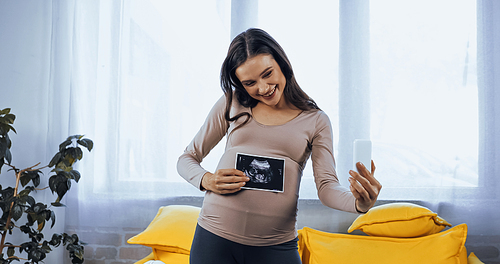 Smiling pregnant woman holding ultrasound scan of baby during video chat
