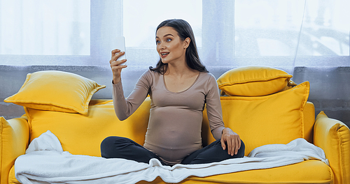 Amazed pregnant woman talking during video call at home
