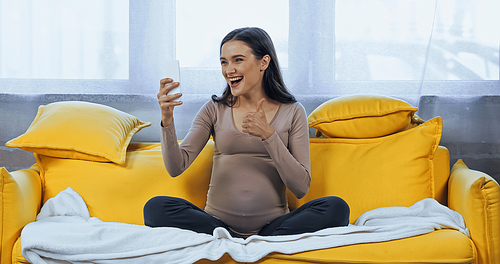 Cheerful pregnant woman showing like during video call on smartphone
