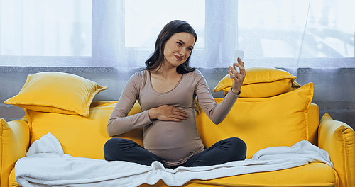 Smiling pregnant woman using smartphone during video call on couch