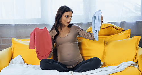 Pregnant woman looking at baby bodysuit on couch