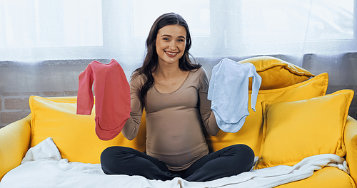 Smiling pregnant woman holding baby clothes and 