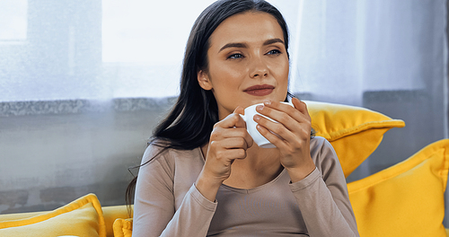 Young woman holding cup of coffee and looking away at home