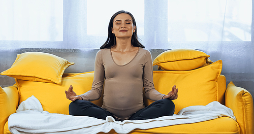 Smiling pregnant woman meditating with closed eyes on couch