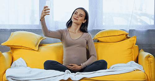 Smiling pregnant woman posing for selfie at home