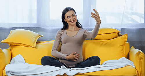 Cheerful pregnant woman taking selfie on smartphone at home