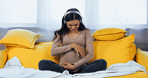 Pregnant woman in headphones looking at belly on couch