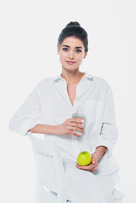 Pretty woman with glass of water and organic apple sitting on chair isolated on white