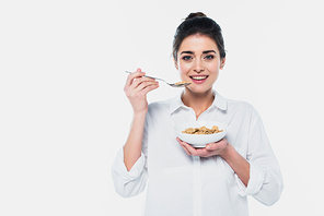 Smiling brunette woman holding spoon and bowl of cereals isolated on white
