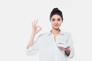 Positive brunette woman with bowl of cereals showing okay gesture isolated on white