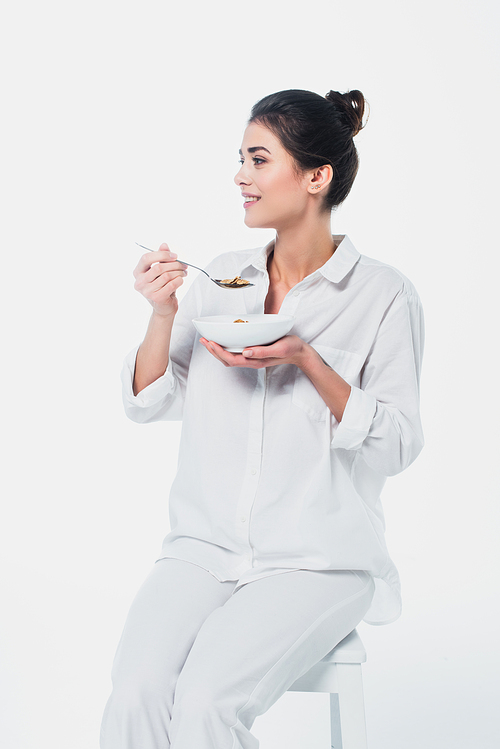 Smiling woman holding bowl of cereals and spoon on chair isolated on white
