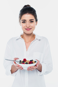 Smiling woman holding bowl of cereals and berries isolated on white