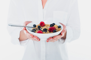 Cropped view of bowl of cereals and fresh berries in hands of young woman isolated on white