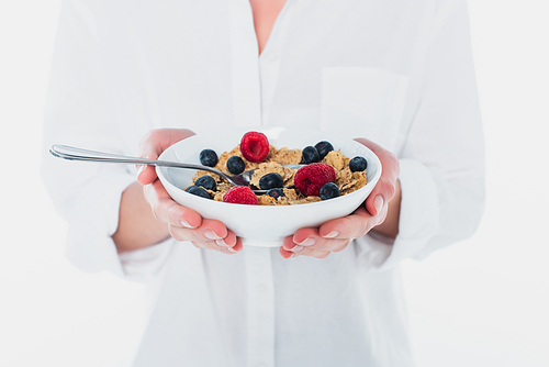 Cropped view of bowl of cereals and fresh berries in hands of young woman isolated on white