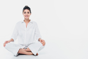 Cheerful woman sitting in yoga pose and smiling at camera on white background