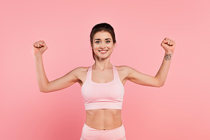 Cheerful sportswoman showing muscles isolated on pink