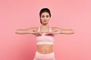 Young fit sportswoman exercising on pink background