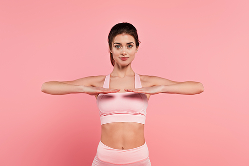 Young fit sportswoman exercising on pink background
