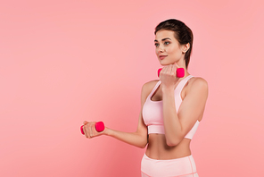 Woman in sportswear training with pink dumbbells isolated on pink