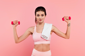 Young sportswoman with towel exercising with dumbbells isolated on pink