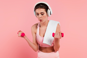 Sportswoman in headphones training with dumbbells isolated on pink