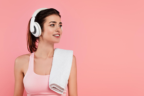 Positive sportswoman in headphones with towel isolated on pink