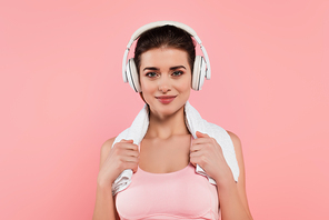Brunette sportswoman in headphones holding towel isolated on pink
