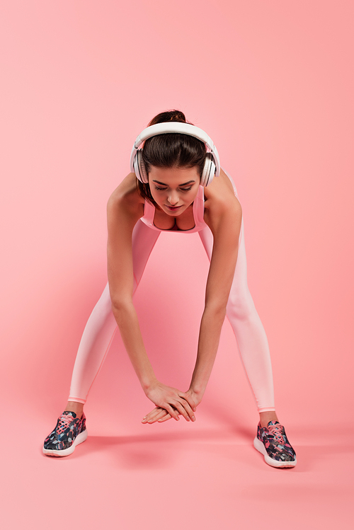 Sportswoman in headphones warming up while training on pink background