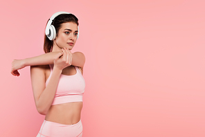 Woman in headphones stretching isolated on pink