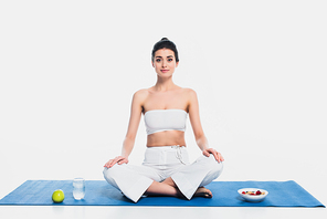 Woman in yoga pose sitting near apple, glass of water and cereals on white background