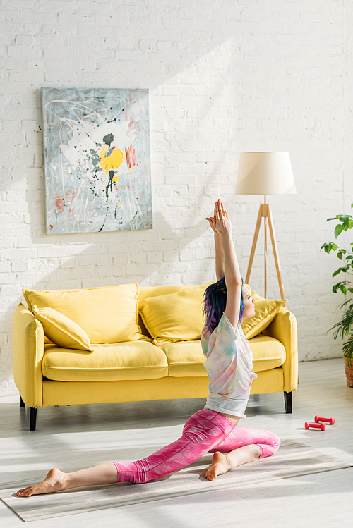 Woman with colorful hair in pigeon pose on yoga mat in living room