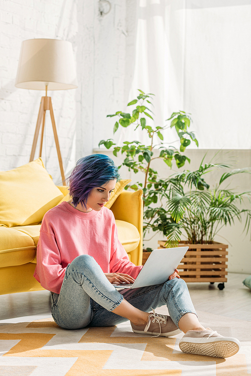 Freelancer with colorful hair working with laptop on floor in living room