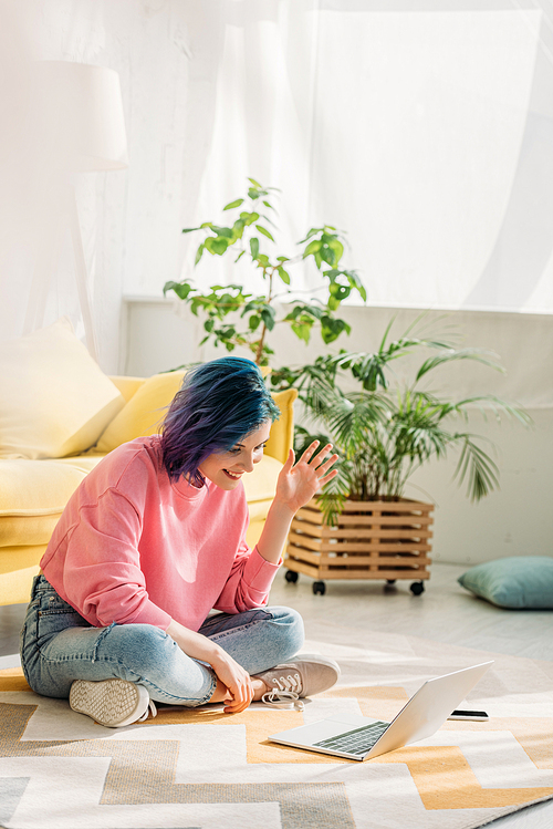 Girl with colorful hair waving hand, smiling and making video call on floor