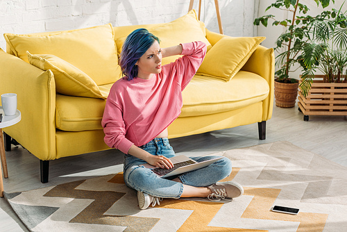 Thoughtful freelancer with colorful hair working with laptop near smartphone on floor