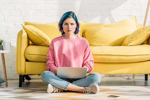 Freelancer with colorful hair and crossed legs  and working with laptop near sofa in living room