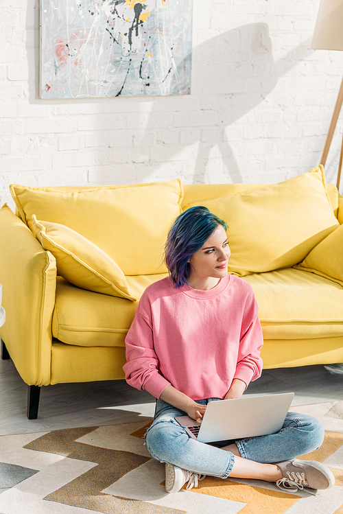 High angle view of thoughtful freelancer with colorful hair looking away and working with laptop near sofa on floor