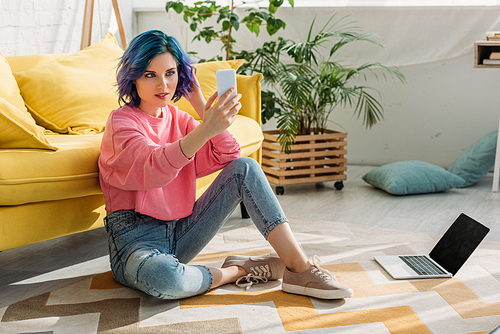 Freelancer with colorful hair taking selfie with smartphone near sofa on floor in living room