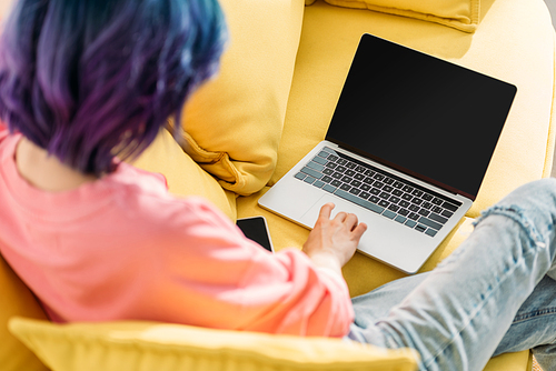 Selective focus of freelancer with colorful hair and laptop sitting on sofa