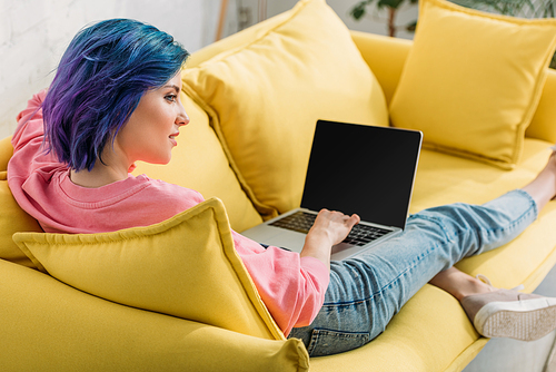 Freelancer with colorful hair and laptop smiling and lying on sofa in living room