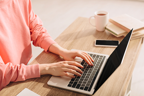 Cropped view of freelancer working with laptop at table