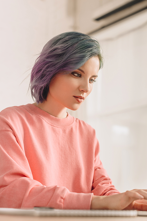 Selective focus of concentrated freelancer with colorful hair in pink sweatshirt at table