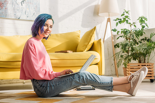 Freelancer with colorful hair smiling,  and working with laptop on floor in living room