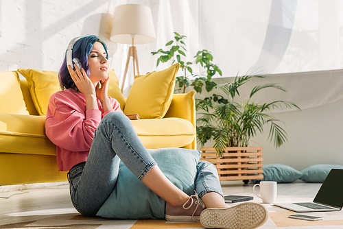 Freelancer in headphones with colorful hair and closed eyes near sofa on floor in living room