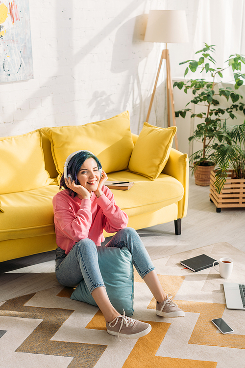 High angle view of freelancer with colorful hair in headphones smiling near sofa on floor in living room